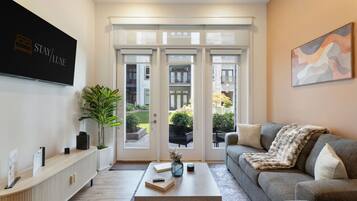 A modern living room with a sofa, a coffee table, a TV, and a large window with a view of the outside.