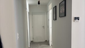 A hallway with a ceiling-mounted air conditioner, a light fixture, and a door at the end.