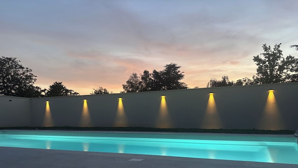 A swimming pool with a light blue tint, surrounded by a low wall with evenly spaced lights.