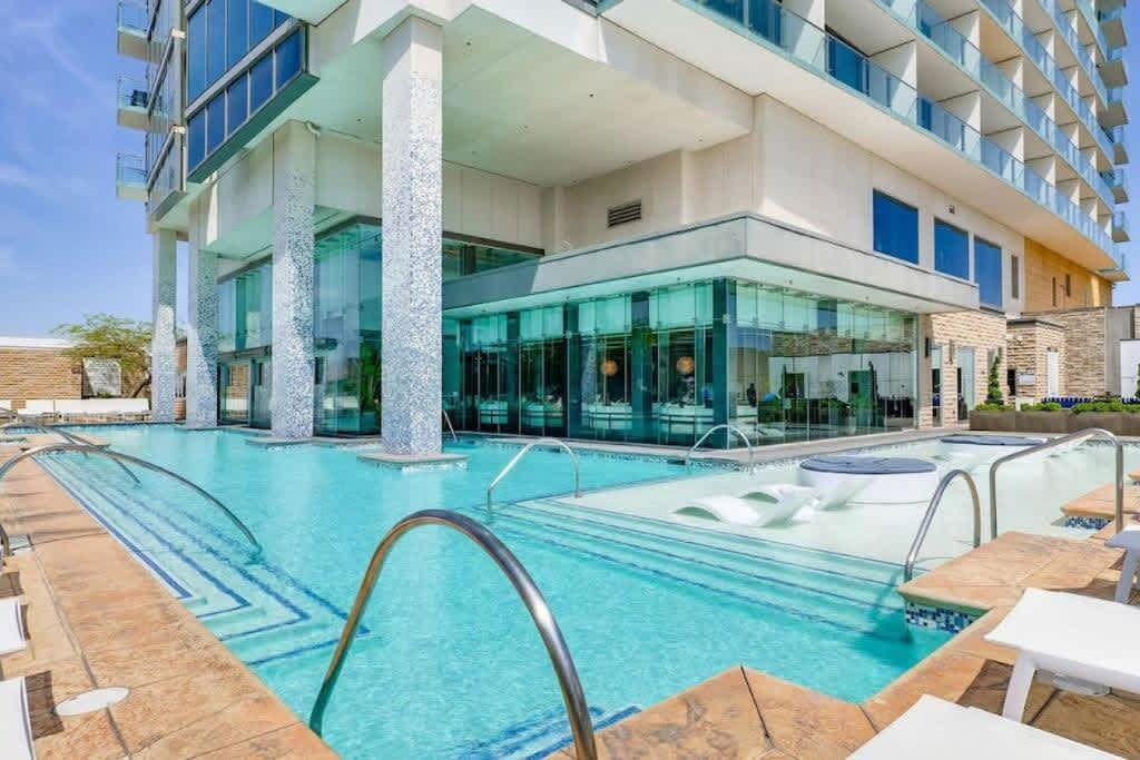 A modern hotel with a swimming pool, outdoor seating, and a glass-enclosed spa area.