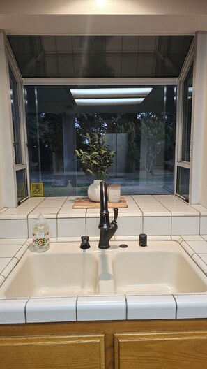 A kitchen with a white sink, a black faucet, a potted plant, and a candle on the counter. - Spacious 4bd 3bth NW Home with AC (Bakersfield)