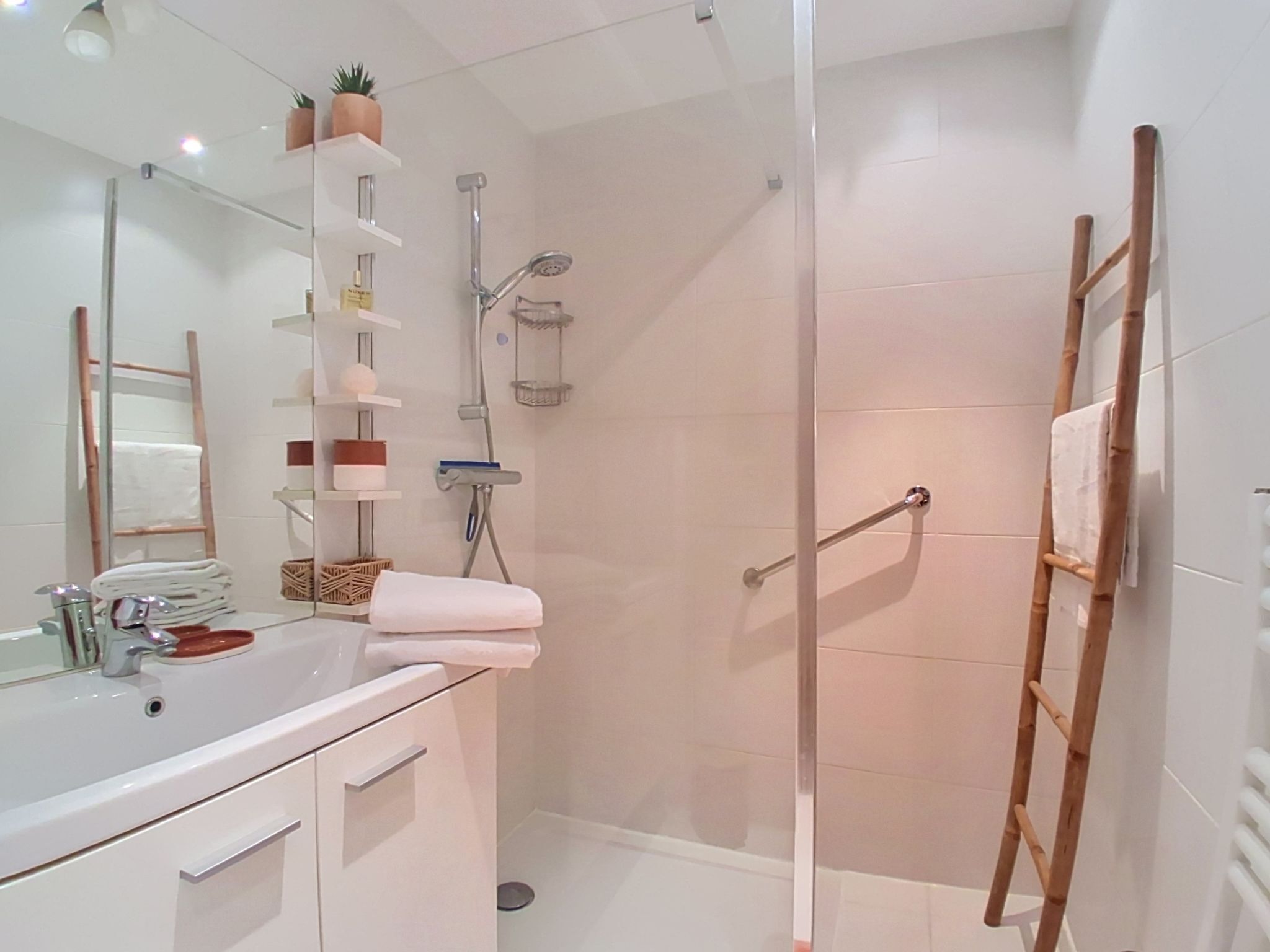 A modern bathroom with a glass shower enclosure, a white sink, and a wooden ladder.
