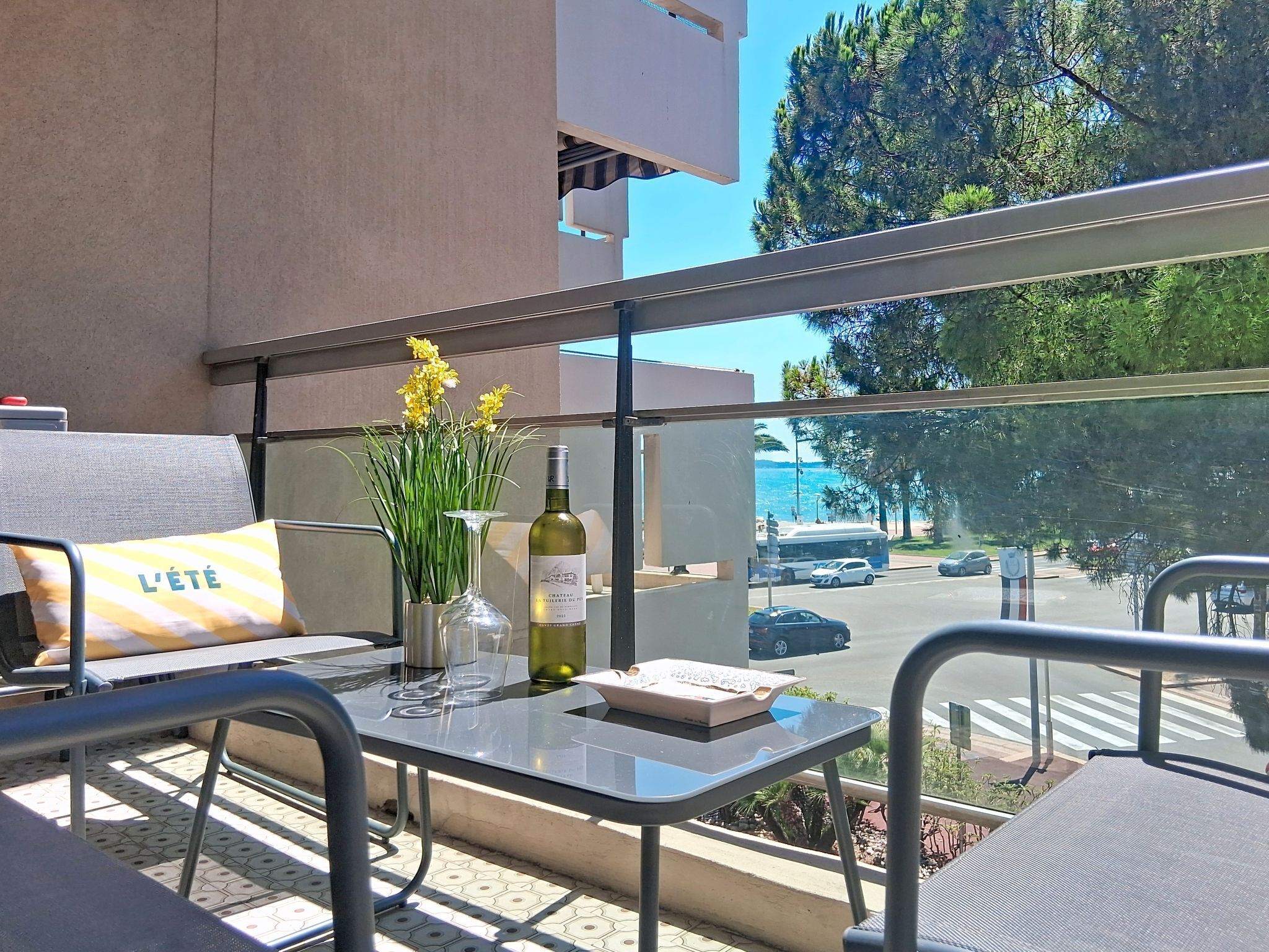 A balcony with a table, a chair, a cushion, a vase with flowers, and a bottle of wine.