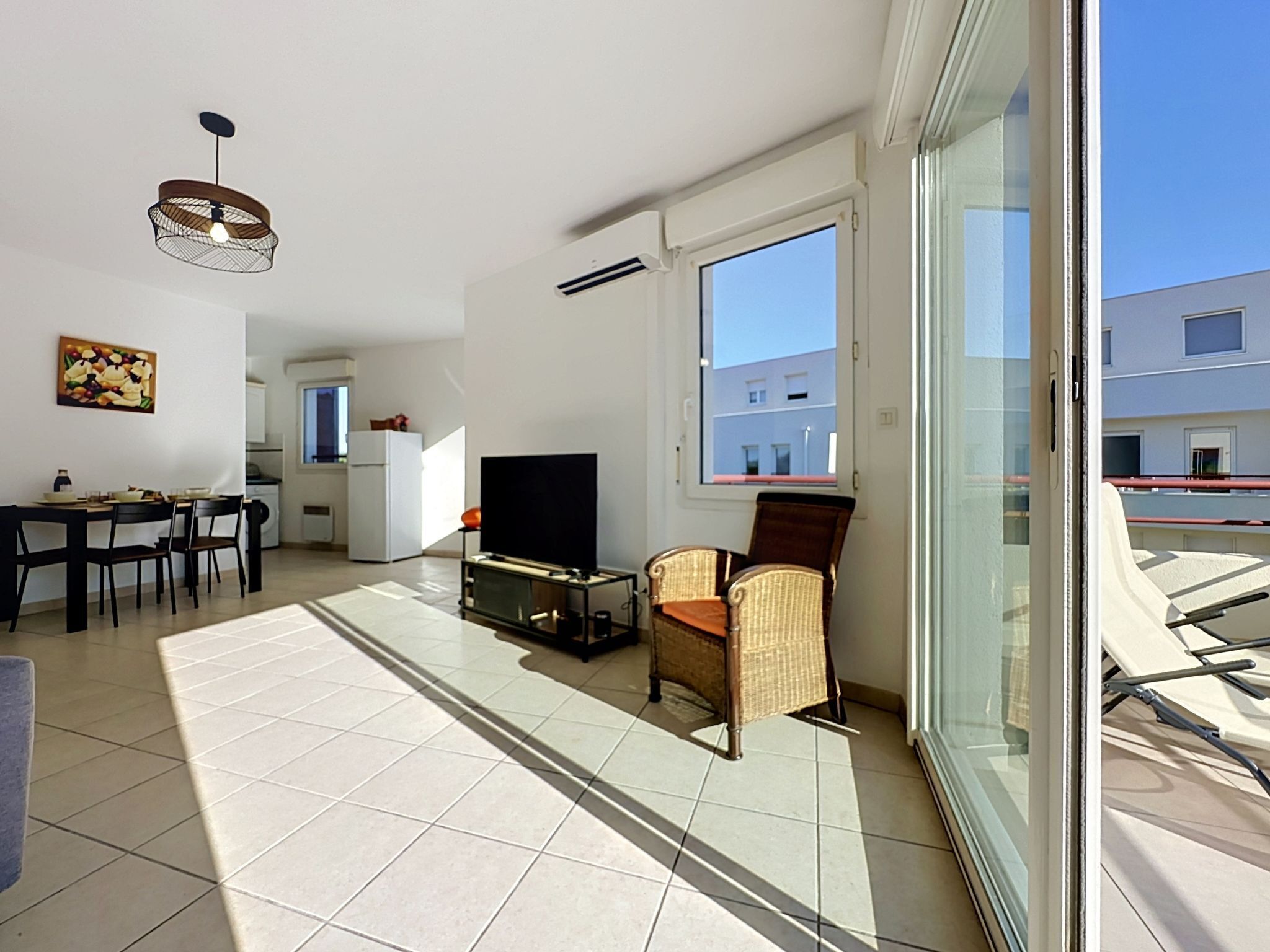 A modern apartment with a dining area, a TV, wicker chairs, and a large window.