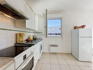 A compact kitchen with a stove, oven, washing machine, and a refrigerator. A window provides a view of a building outside. - L'Hyppocampe by Interhome (Port Camargue)