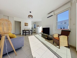 Una sala moderna con sofá, televisor, mesa de comedor y silla de mimbre.
