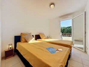 Habitación de hotel con dos camas, una mesita con una lámpara y vistas a zonas verdes a través de una puerta corredera.