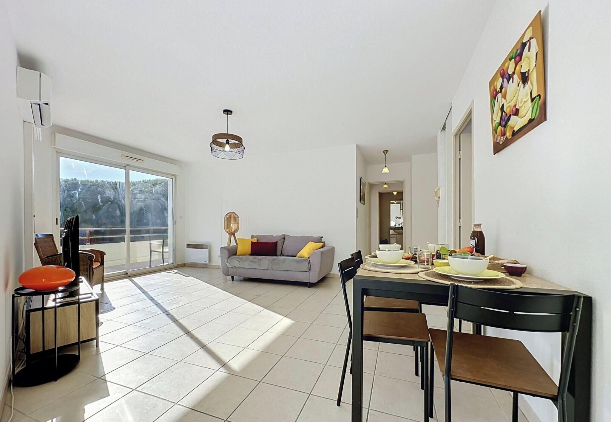 A spacious living area with a sofa, dining table, chairs, and a large window.