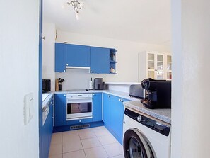 Eine kompakte Küche mit blauen Schränken, einem eingebauten Backofen, einer Mikrowelle, einer Kaffeemaschine und einer Waschmaschine.