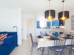 Ein modernes Wohnzimmer mit einem blauen Sofa und einer Essecke mit Tisch für vier Personen.