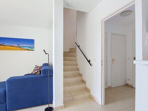A room with a blue sofa, a painting of a beach, a staircase, and a white door. - Les Grenadines by Interhome (Les Issambres)