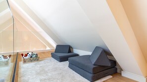 Une chambre de style loft moderne, avec un plafond en pente, une grande fenêtre et un coin salon confortable agrémenté de coussins.