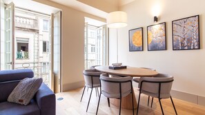 Ein modernes Wohnzimmer mit einem runden Tisch und vier Stühlen, einer Couch mit einem Zierkissen sowie drei gerahmten Kunstwerken an der Wand.
