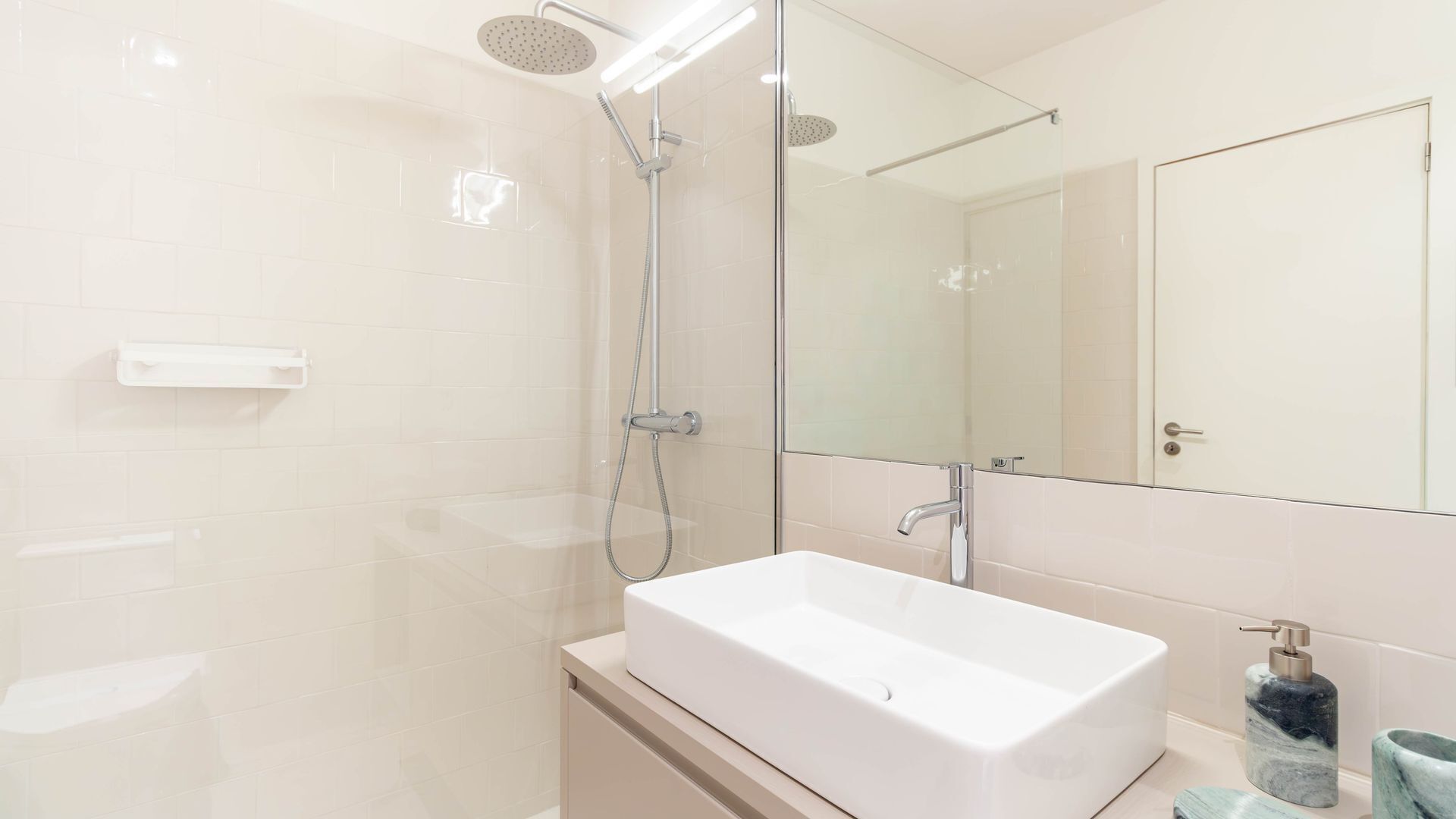 Un baño moderno con ducha a ras de suelo, lavamanos independiente y un espejo grande.