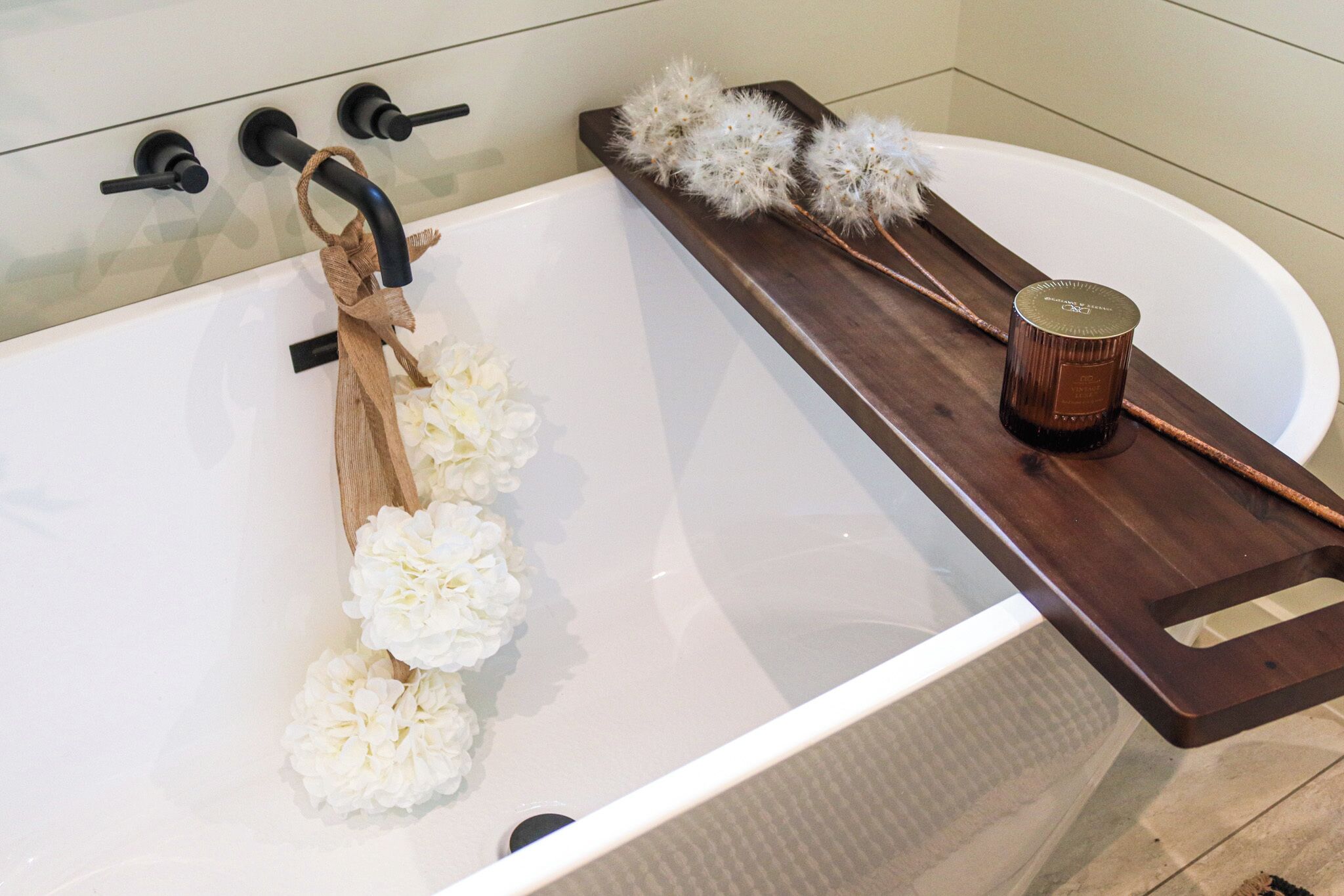 A bathtub with a wooden tray, a candle, and white flowers.