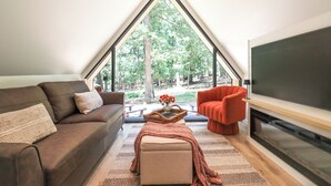 Een gezellige kamer met een bruine bank, een rode fauteuil, een flatscreen televisie en een groot raam met uitzicht op bomen.