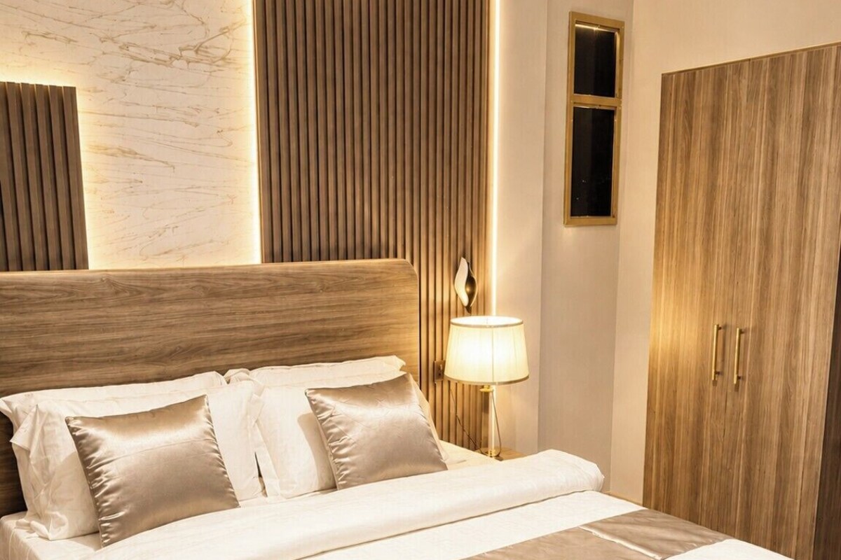 A neatly made bed with a headboard, a bedside lamp, and a wooden wardrobe.
