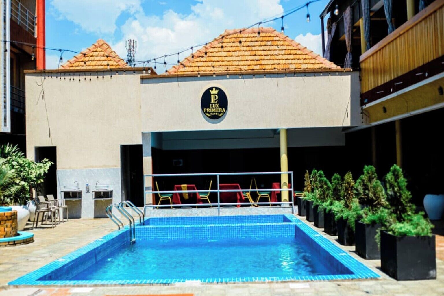 A hotel with a swimming pool, outdoor seating, and a sign reading 'LUX PRIMER HOTEL.'