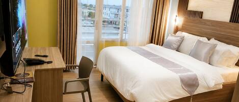 Quarto de hotel com cama, escrivaninha, cadeira, televisão e vista para a cidade.
