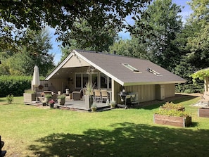 Ein einstöckiges Haus mit überdachter Terrasse, Gartenmöbeln und einem Grill.