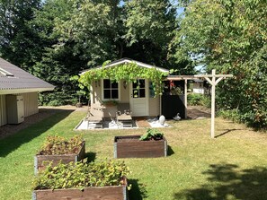 Ein kleines Holzhaus mit Veranda, umgeben von einem gepflegten Rasen und Blumenbeeten.