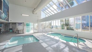 An indoor swimming pool with clear glass walls, a lifeguard station, and a view of palm trees outside. - Posh Piper: 2BD, 2BA Oceanfront Condo in Royal Garden Resort, Garden City (Murrells Inlet)