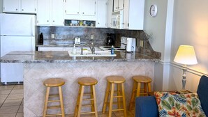 A compact kitchen with white cabinets, a central island with stools, a refrigerator, and a microwave. - Posh Piper: 2BD, 2BA Oceanfront Condo in Royal Garden Resort, Garden City (Murrells Inlet)