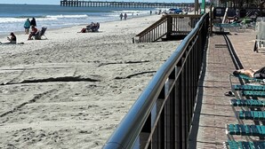 A beach with a pier in the distance, a walkway with chairs, and a building with balconies. - Posh Piper: 2BD, 2BA Oceanfront Condo in Royal Garden Resort, Garden City (Murrells Inlet)