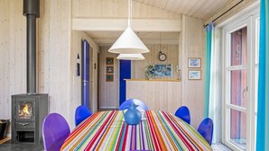 Um quarto com lareira a lenha, toalha de mesa listrada e cadeiras azuis.