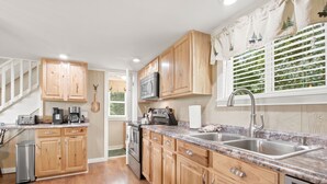 A kitchen with wooden cabinets, a microwave, a sink, and a staircase. - Romantic Mountain Retreat with Fenced Yard & Views (Creston)