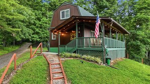 A rustic cabin with a porch, a wooden staircase, and an American flag. - Romantic Mountain Retreat with Fenced Yard & Views (Creston)