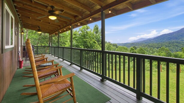 A covered porch with wooden rocking chairs, a green mat, and a view of a mountainous landscape. - Romantic Mountain Retreat with Fenced Yard & Views (Creston)