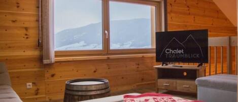 A wooden-paneled room with a bed, a television, and a window with a view of mountains.