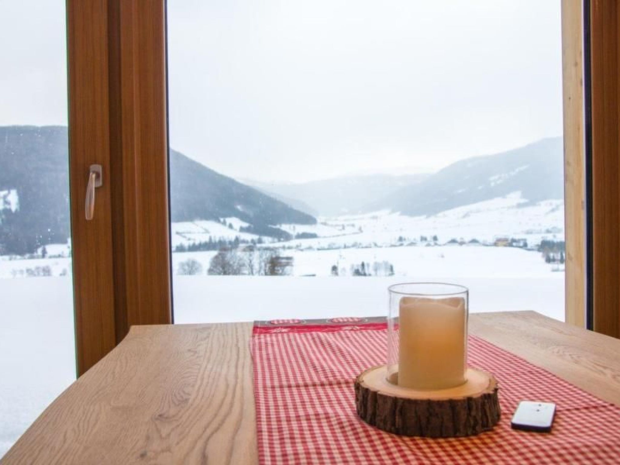 Ein Holztisch mit einem Getränk, einer karierten Tischdecke und einem Smartphone auf einem Untersetzer aus Holz.