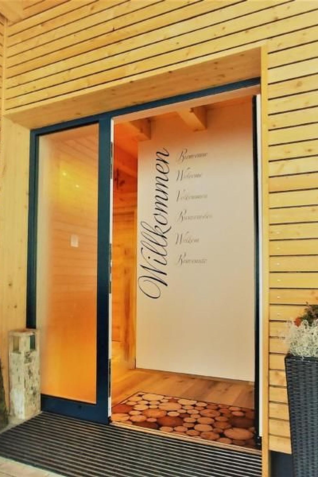 A wooden building entrance with a welcome sign and a small step leading into the building.