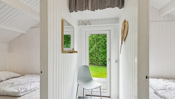 A bedroom with two beds, a white chair, a door leading outside, and a mirror on the wall. - "Maini" - 30km from the sea by Interhome (Toftlund)