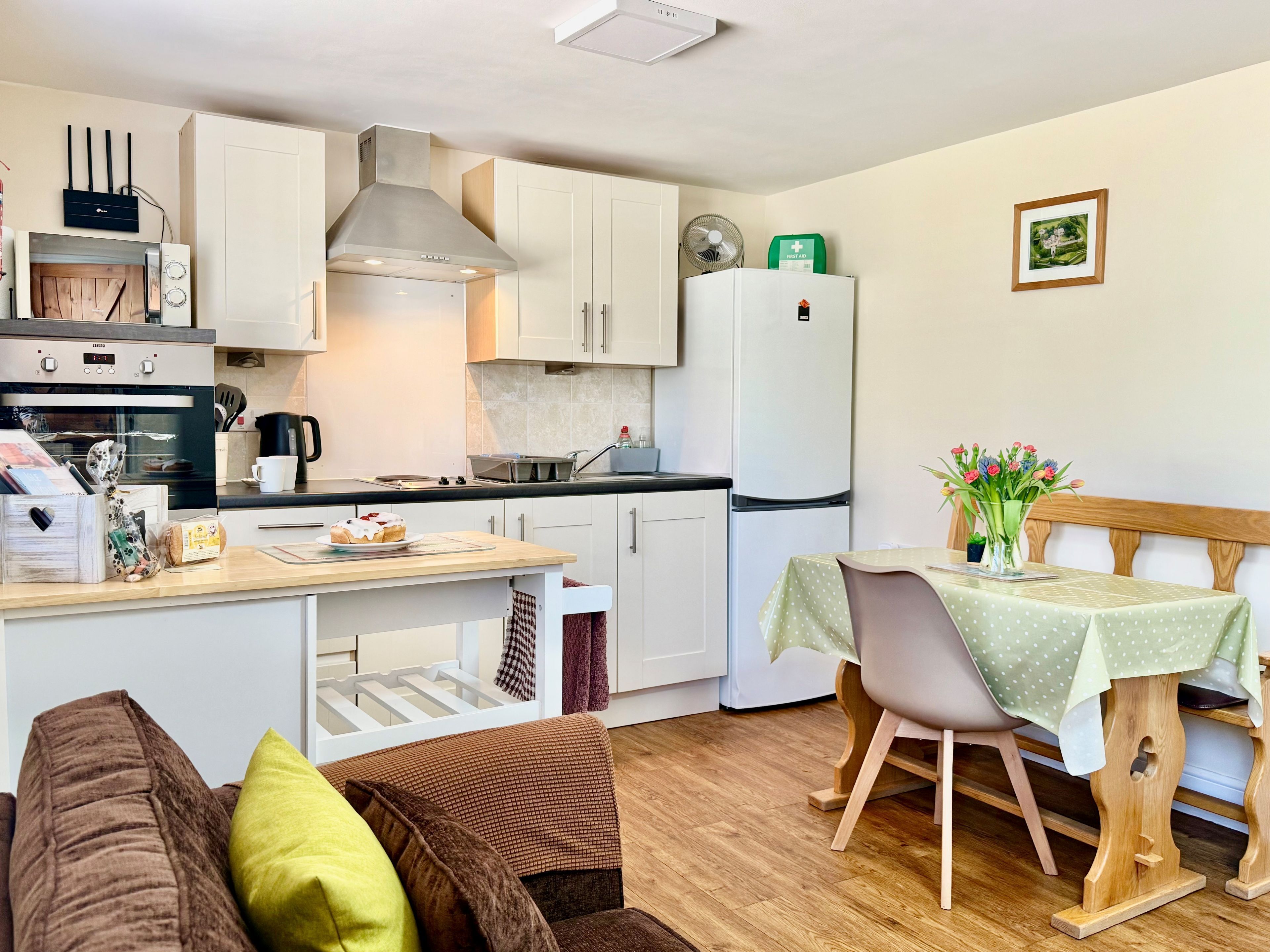 Una cocina compacta con armarios blancos, horno empotrado, refrigerador blanco y una zona de comedor con una mesa y sillas pequeñas.