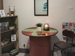 A round table with a candle, a small plant, and a notebook. There is a bookshelf with books and decorative items. - Ortigas CBD Budget Stays (Mandaluyong City)