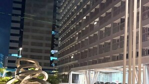 Un edificio moderno con varios pisos y balcones, un estacionamiento bien iluminado y una escultura de metal en primer plano.