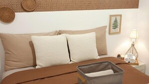 Una cama bien hecha con una colcha marrón, dos almohadas color beige y un caja de almacenamiento gris sobre la cama.