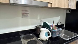 Una kitchenette con extractor de acero inoxidable, un hervidor blanco, una olla y un escurreplatos con utensilios.