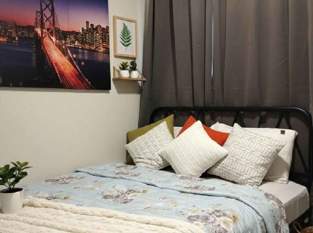 A bedroom with a bed, pillows, a blanket, a potted plant, a cityscape painting, and a curtain.