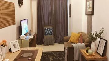 Una sala de estar con sofá, mesa de centro, televisor y cortina.