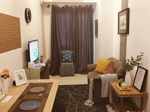 Un salon avec un canapé, une table basse, un téléviseur et un rideau.