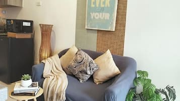 Una sala de estar con un sofá, una mesita con una planta, una radio y un cartel.