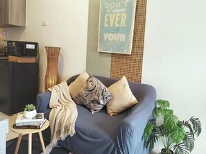A living room with a sofa, a small table with a plant, a wall-mounted radio, and a poster. - Ortigas CBD Budget Stays (Mandaluyong City)
