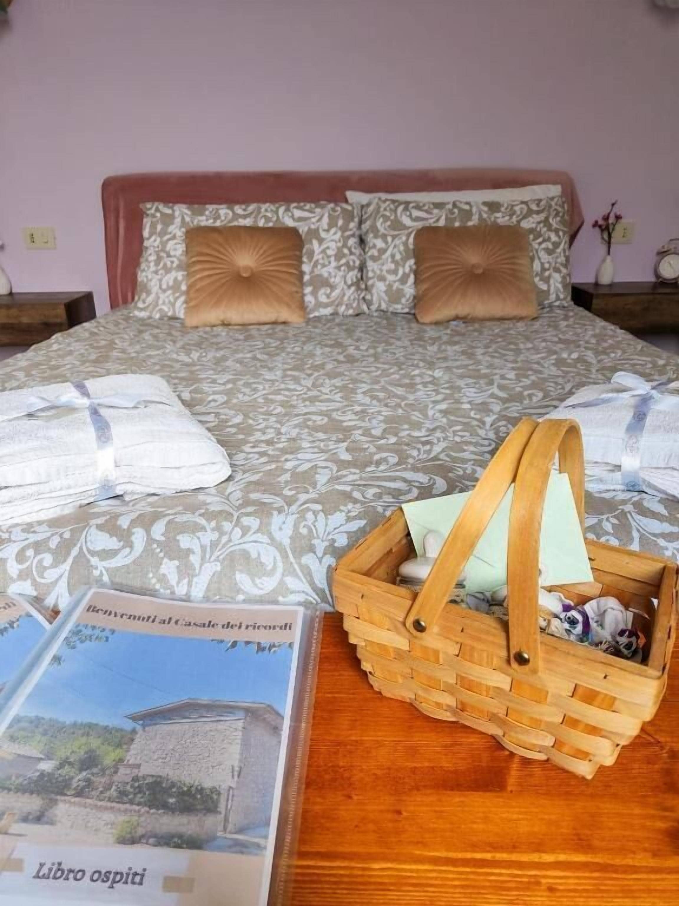 Una cama bien tendida con ropa de cama estampada, una mesita de noche de madera con una cesta, y un libro titulado 'Libro ospiti' sobre la mesa.