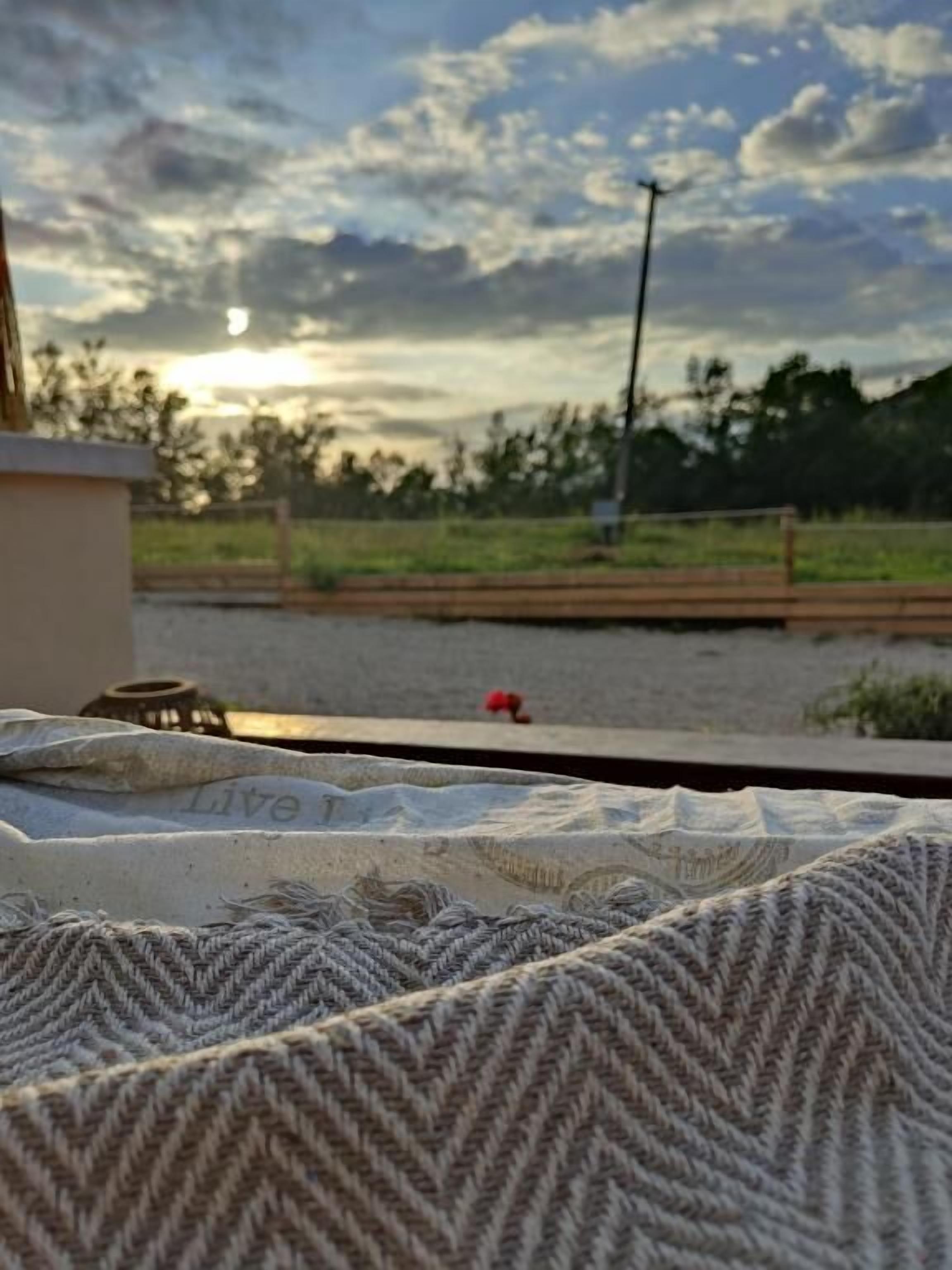Vista des d'una finestra amb una manta estampada, una tanca de fusta i un camp al fons.