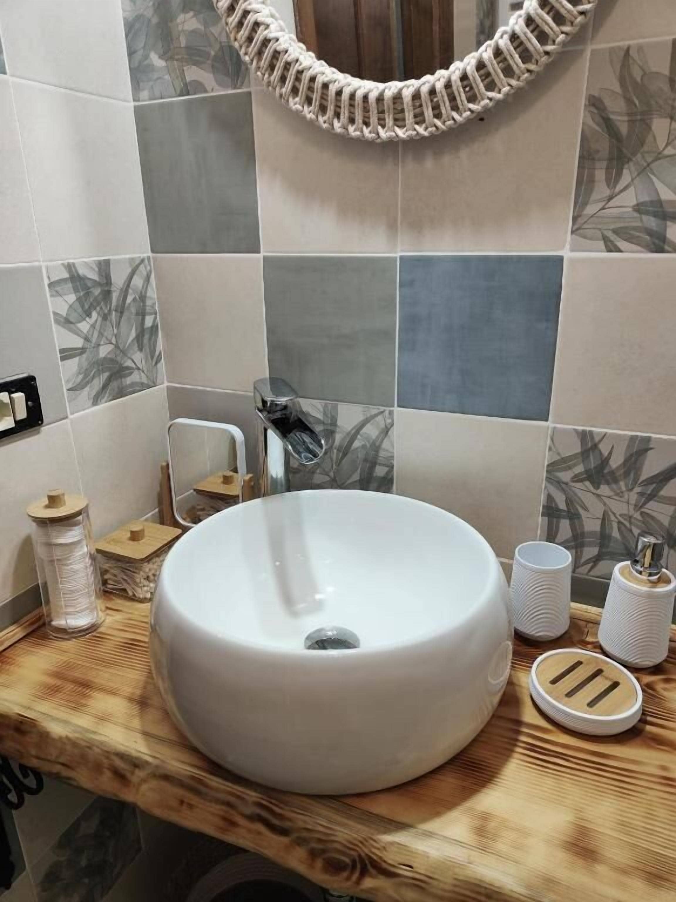 A bathroom with a round white sink, a wooden countertop, a towel rack, and a mirror with a decorative frame.