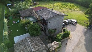 Un edificio de piedra con tejado de tejas, un pequeño jardín y un vehículo estacionado.